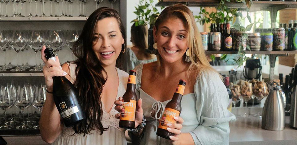 Two women holding beer bottles brewed by The Blind Monk