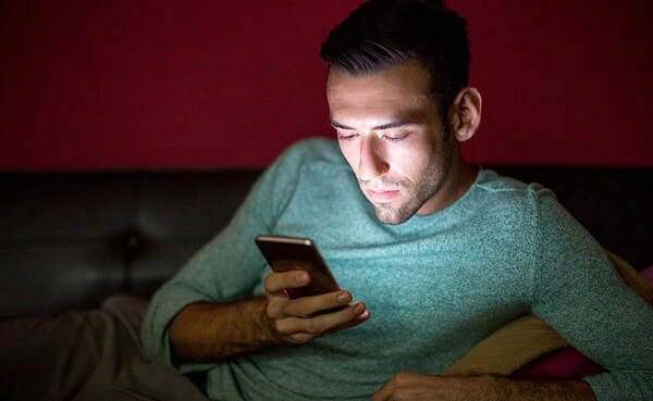 Young man scrolling through dating apps on his phone at midnight, wondering if the next match will deliver real connections.