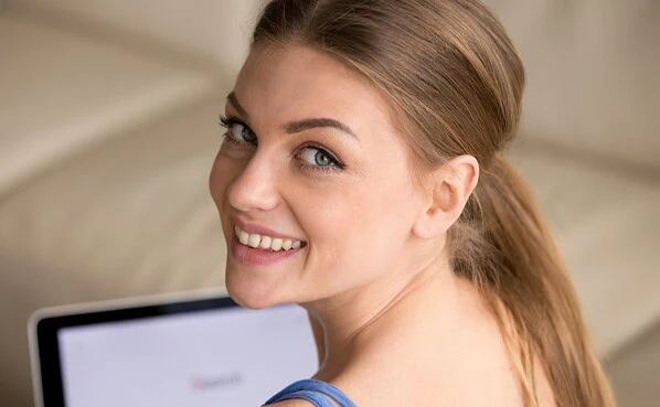 A confident woman smiling warmly during a video call on his laptop in a well-lit room.